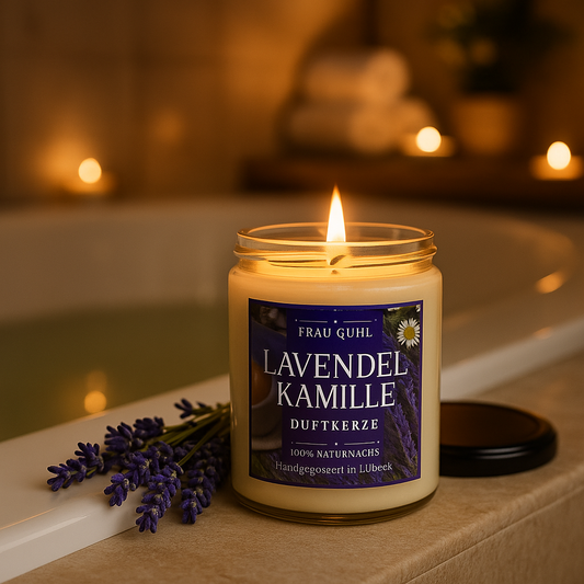Lavendel Kamille Duftkerze von Frau Guhl – handgegossene Kerze im klaren Glas mit Holzdeckel, violettes Etikett, dekoriert mit Lavendel und Kamille.Im Hintergrund eine Badewanne mit angezuendeten Kerzen.